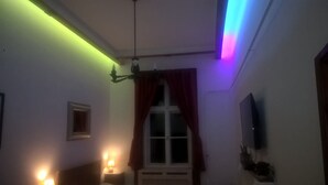 A dimly lit room with a bed, a window with red curtains, a wall-mounted TV, and a small bedside table with a lamp. - Classical Budapest apartment in the old Pest (Budapest)