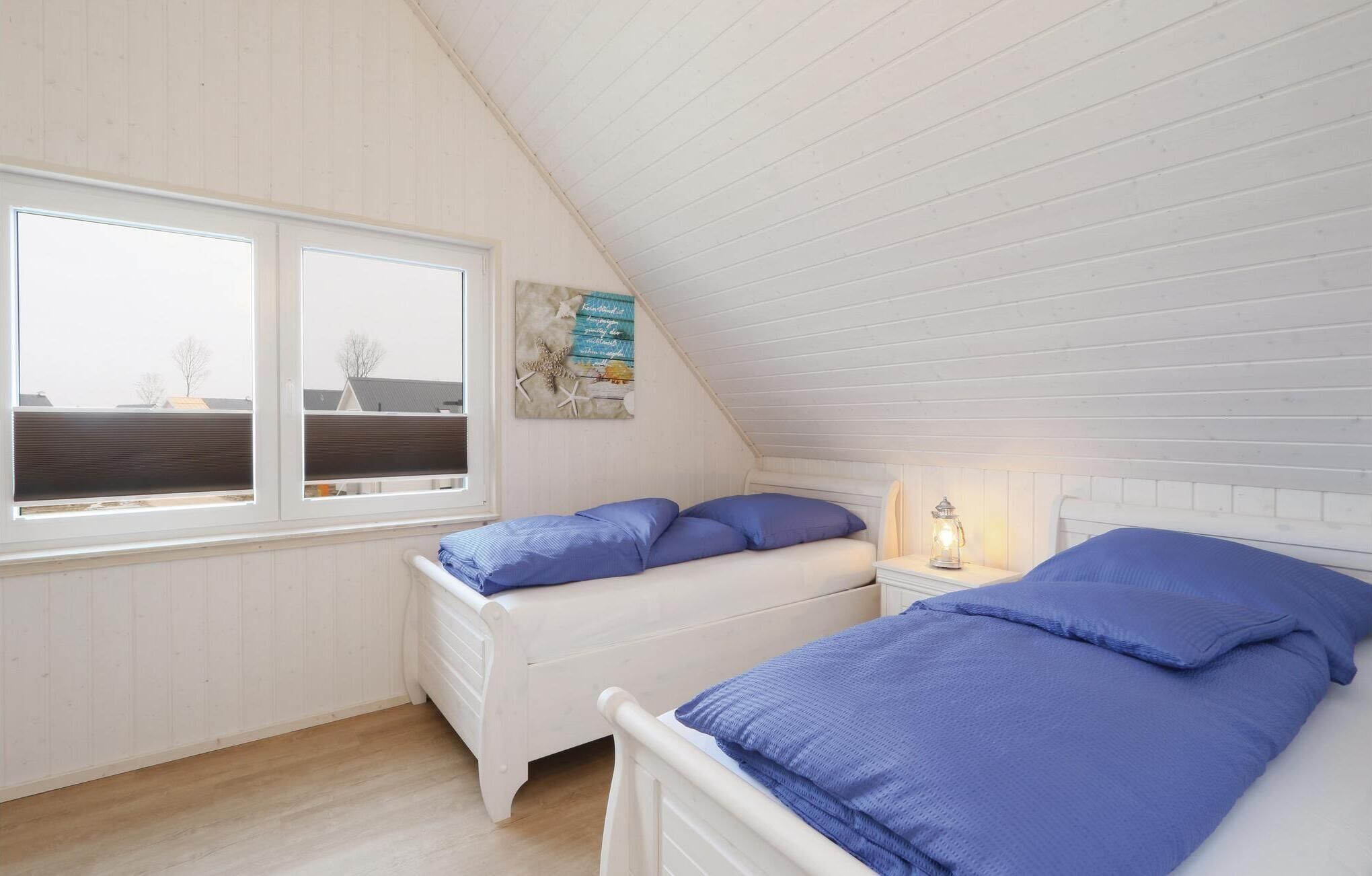 Une petite pièce accueillante avec deux lits blancs, une fenêtre donnant sur des immeubles et un plafond en bois.