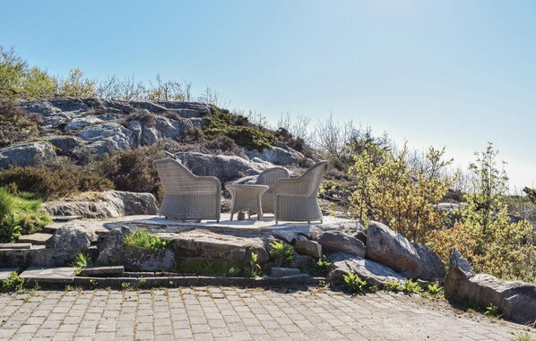 Relax in a serene outdoor setting with wicker chairs and a table amidst the natural beauty of rocky terrain and lush vegetation.