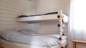 Un llit superposat amb un estovat i coixins de quadres, una taula de fusta i una finestra amb cortines.