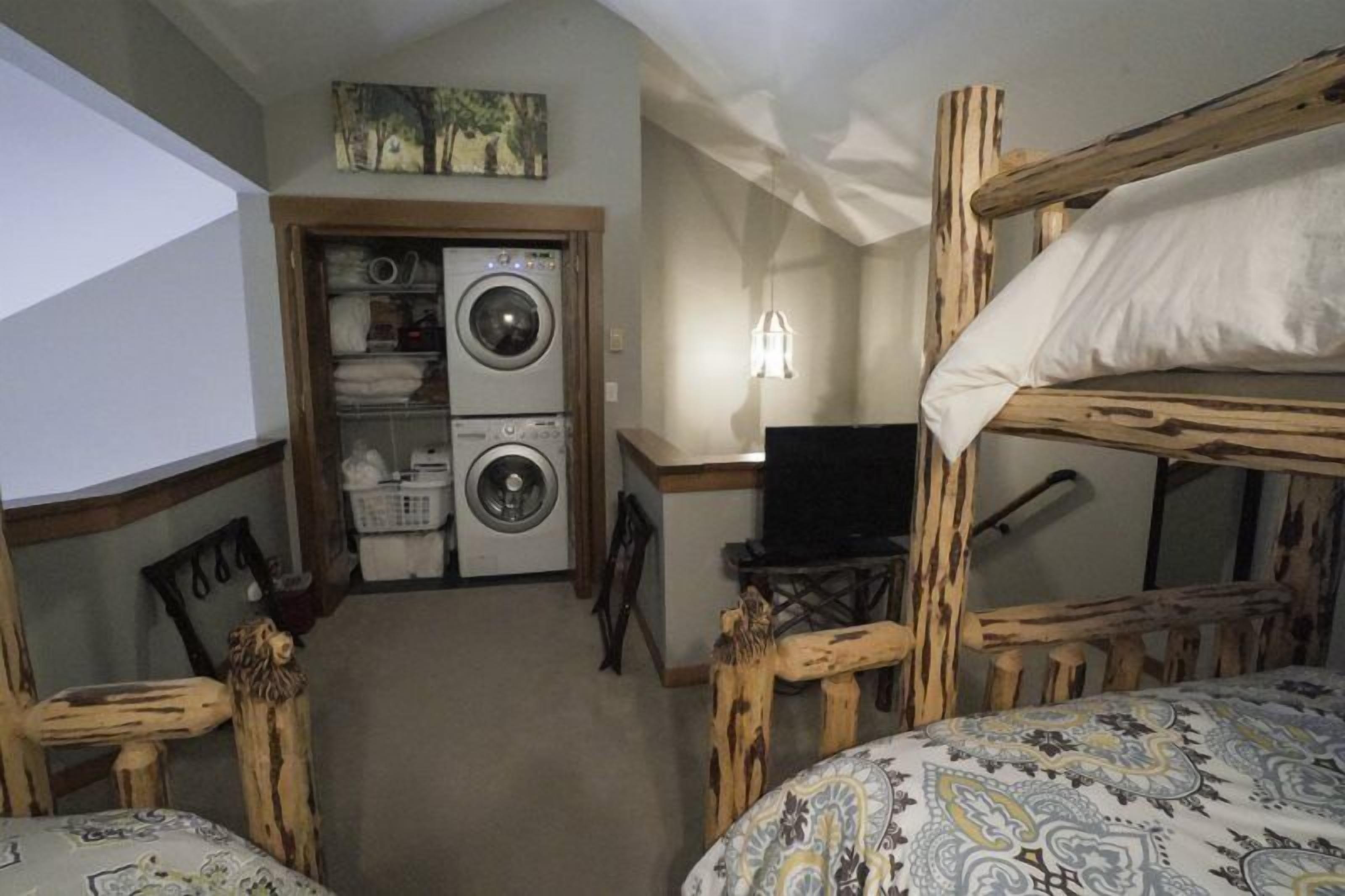 Una habitación con literas, lavadora, escritorio con computadora y silla con diseño de cabeza de león.