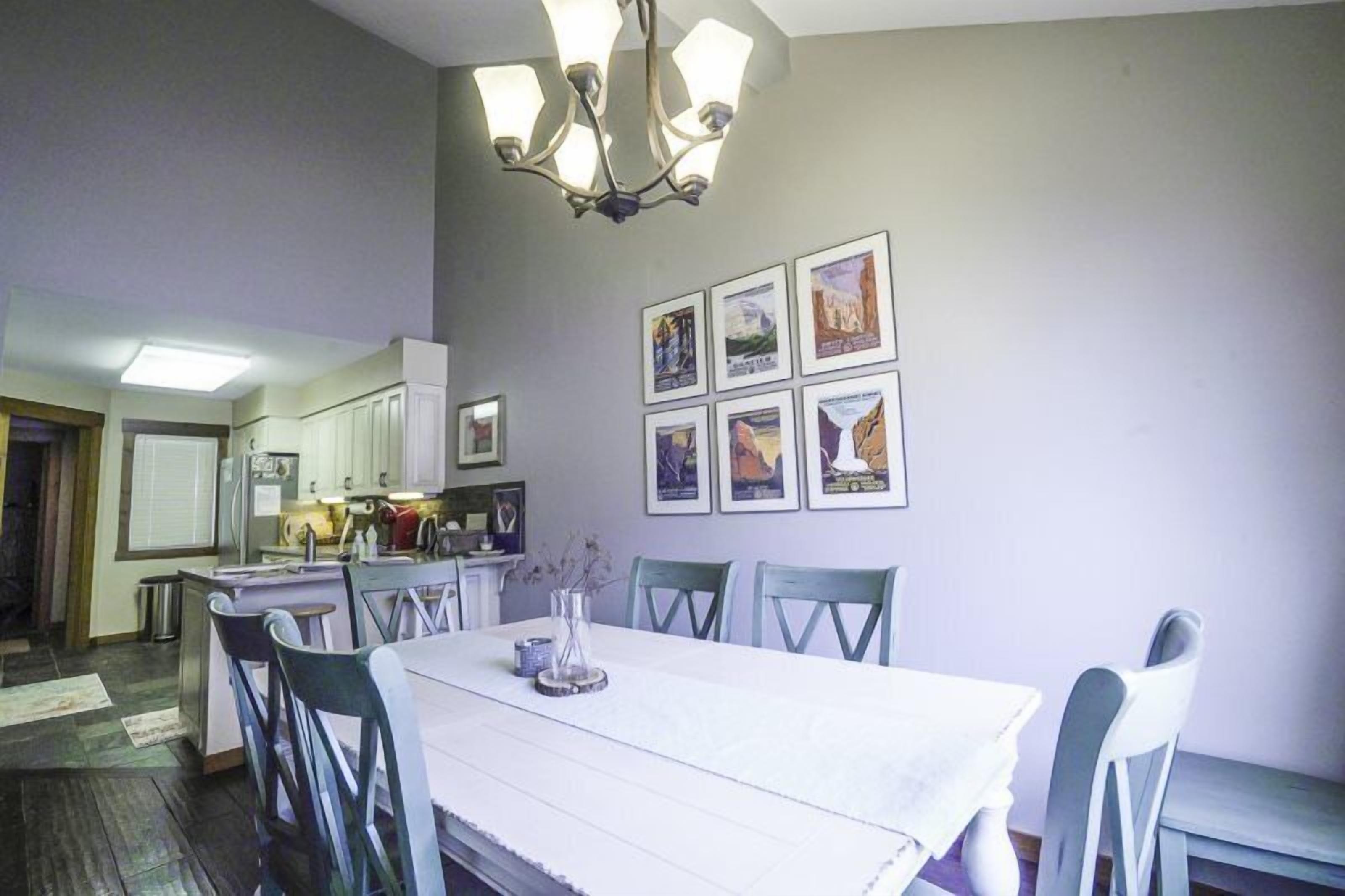 A dining area with a white table, chairs, and a chandelier. There are framed pictures on the wall.