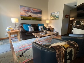A living room with a sofa, coffee table, and chairs, a rug, and paintings on the wall.