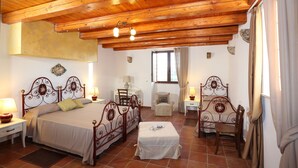 A bedroom with a wooden ceiling, a bed with a headboard, a bedside table, a chair, and a window with curtains. - Serravalle Relais & Country Villa (Chiaramonte Gulfi)