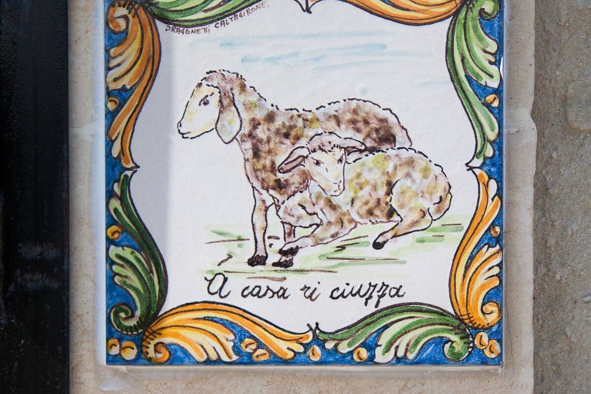 Piastrella in ceramica con illustrazione di una pecora e di un agnello, circondata da motivi decorativi.
