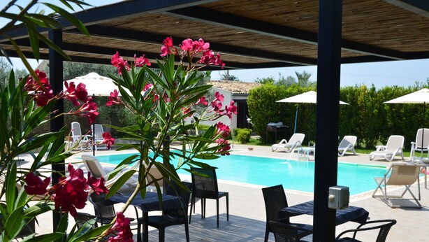 A poolside area with lounge chairs and a table, surrounded by a wooden pergola and lush greenery. - Serravalle Relais & Country Villa (Chiaramonte Gulfi)
