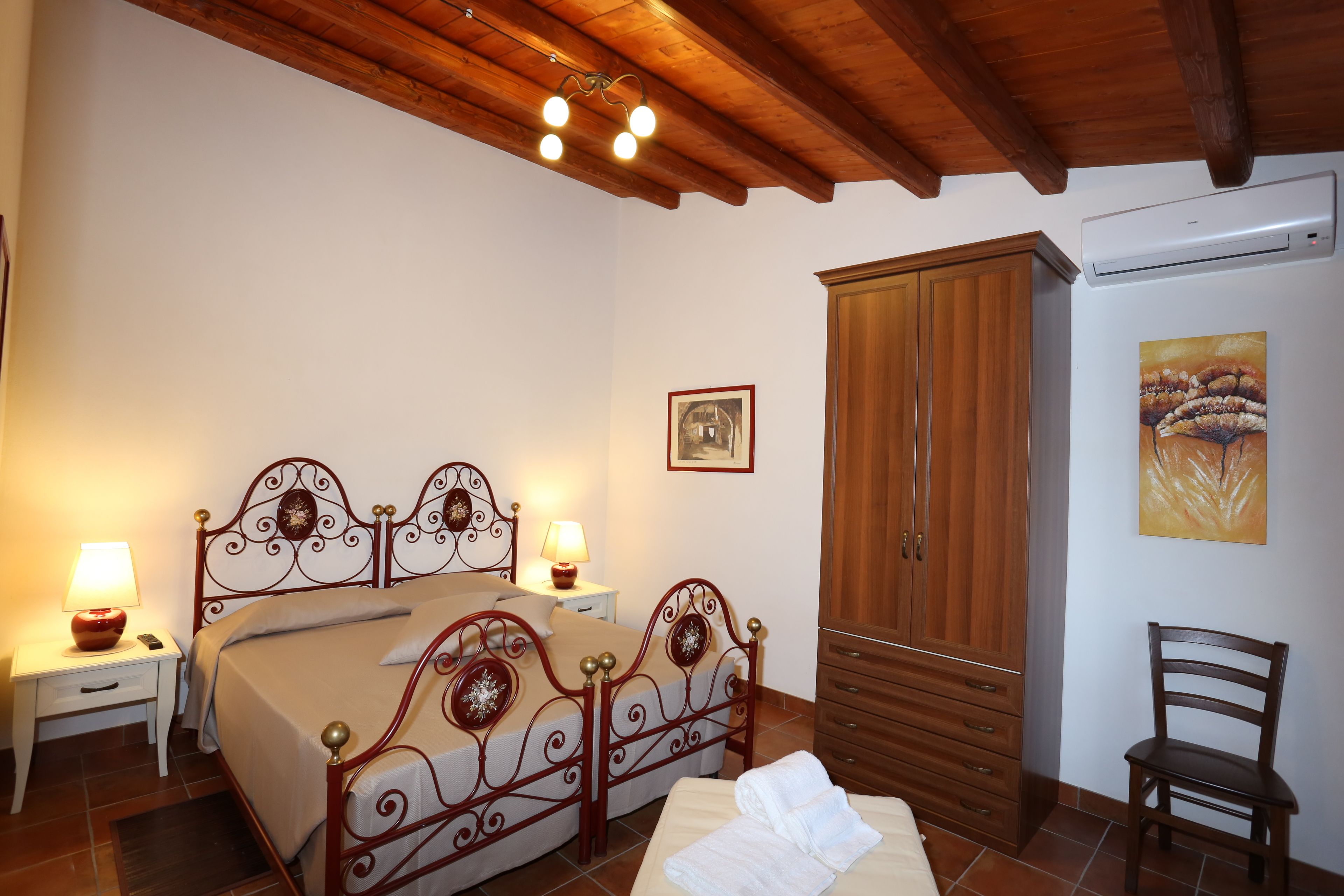 Un dormitori amb llit doble, armari de fusta, taules de nit amb làmpades i un quadre a la paret.