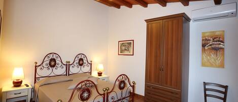 A bedroom with a double bed, wooden wardrobe, bedside tables with lamps, and a painting on the wall.