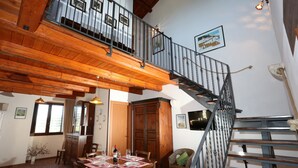 A spacious dining area with a wooden table set for a meal, a staircase with a metal railing, and a view of the upper floor. - Serravalle Relais & Country Villa (Chiaramonte Gulfi)