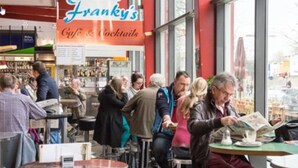 Ein belebtes Café mit Tischen, Stühlen und einer Speisekarte, außerdem ein großes Fenster.