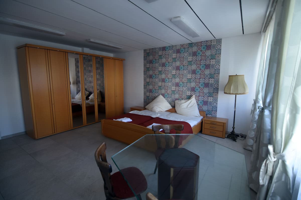Een slaapkamer met een bed, garderobe, nachtkastje, lamp en een glazen tafel met stoelen.