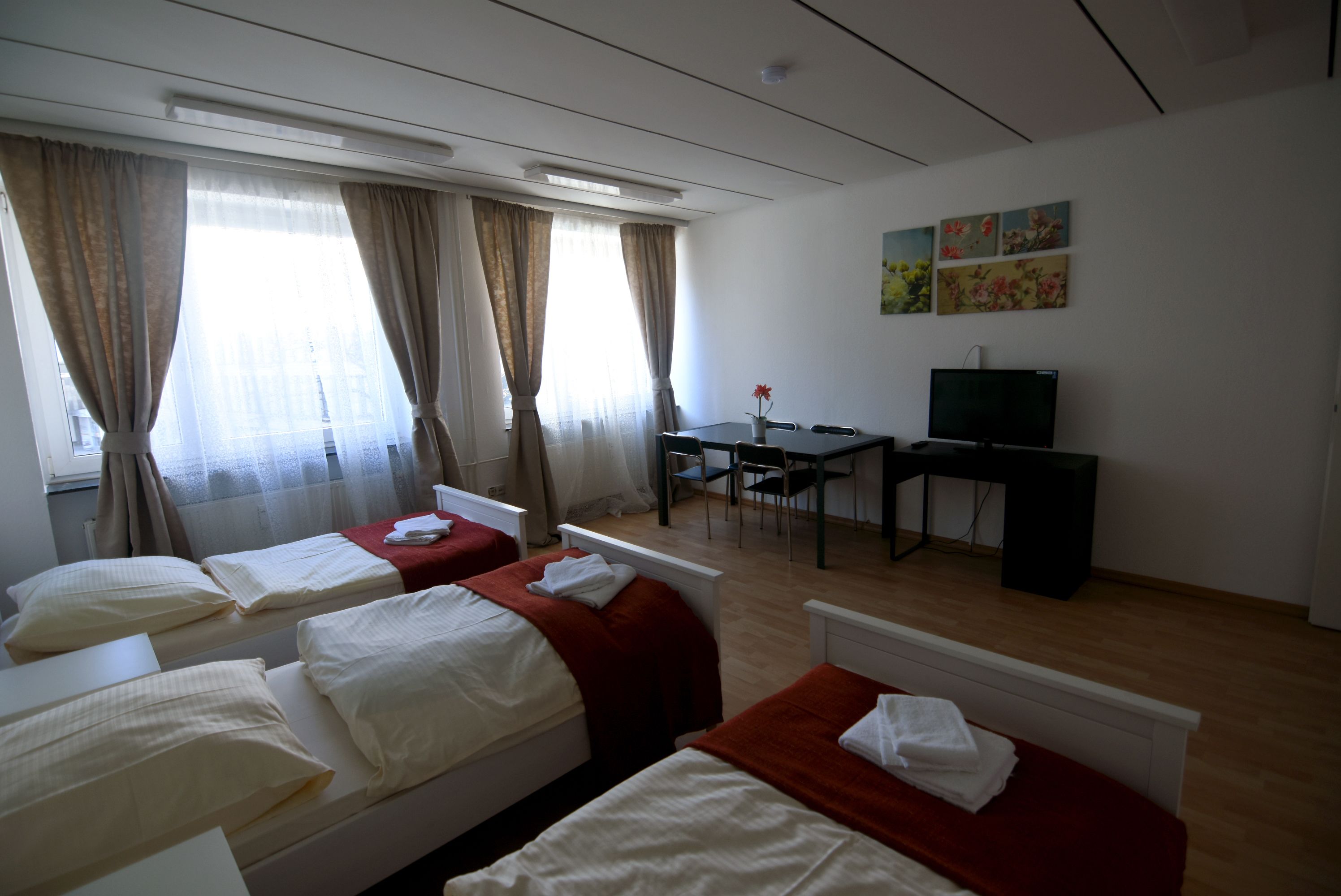 A hotel room with two beds, a desk, a chair, a television, and a window with curtains.