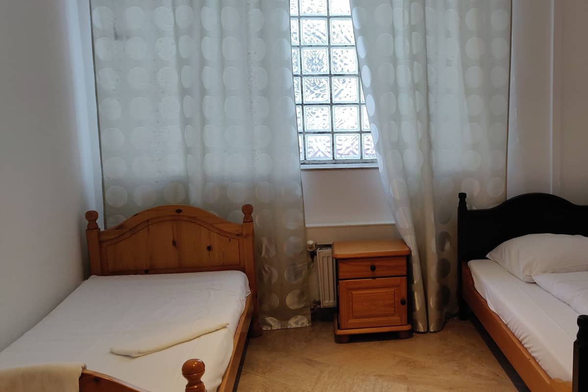 Een slaapkamer met twee houten bedden, een nachtkastje en een raam met gordijnen met een patroon.
