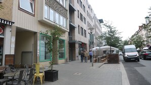 Eine Straße mit einer Reihe von Gebäuden, Außenbestuhlung und einem Lieferwagen.