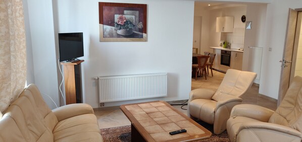 A living room with beige leather chairs, a coffee table with a remote, a flat-screen TV, and a painting on the wall. - Bed Budget City Center Hannover - Hostel (Hannover)