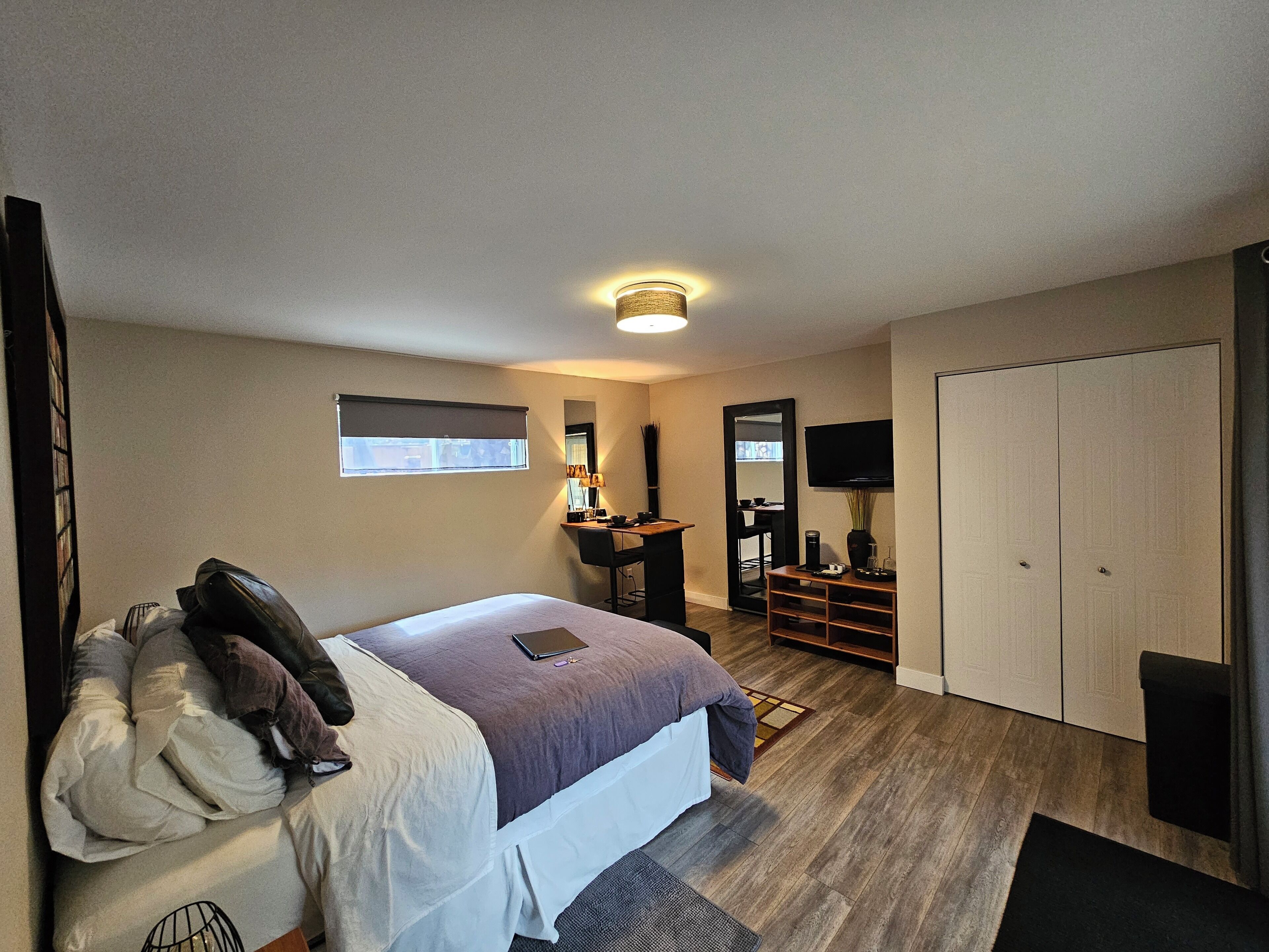 A modern bedroom with a bed, bedside table, mirror, and a TV.
