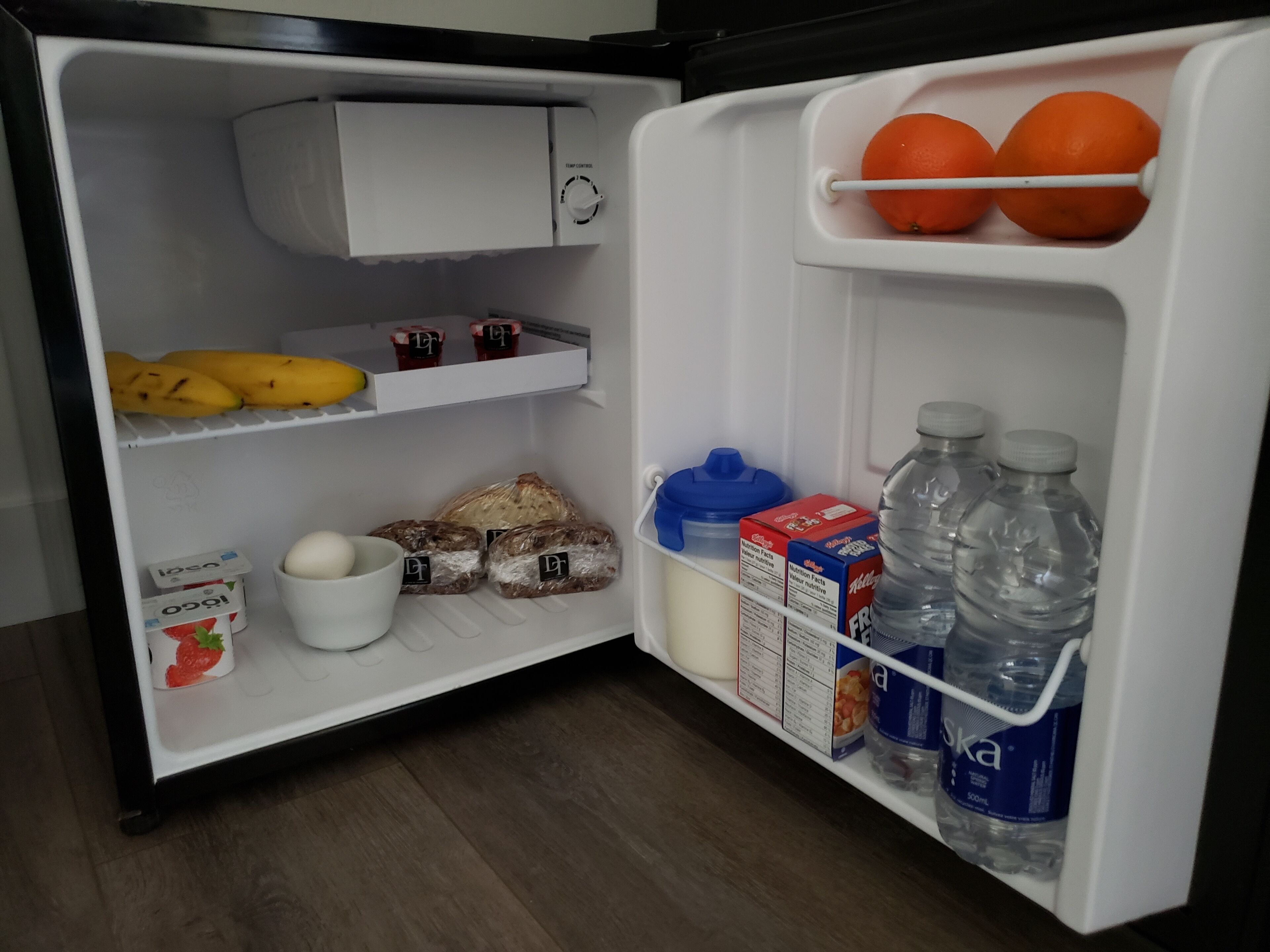 Een koelkast met bananen, brood, eieren, melk en waterflessen.