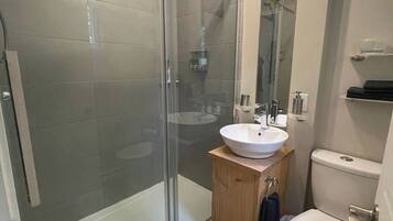 Un baño moderno con cabina de ducha de vidrio, tocador de madera con lavabo blanco y váter blanco.