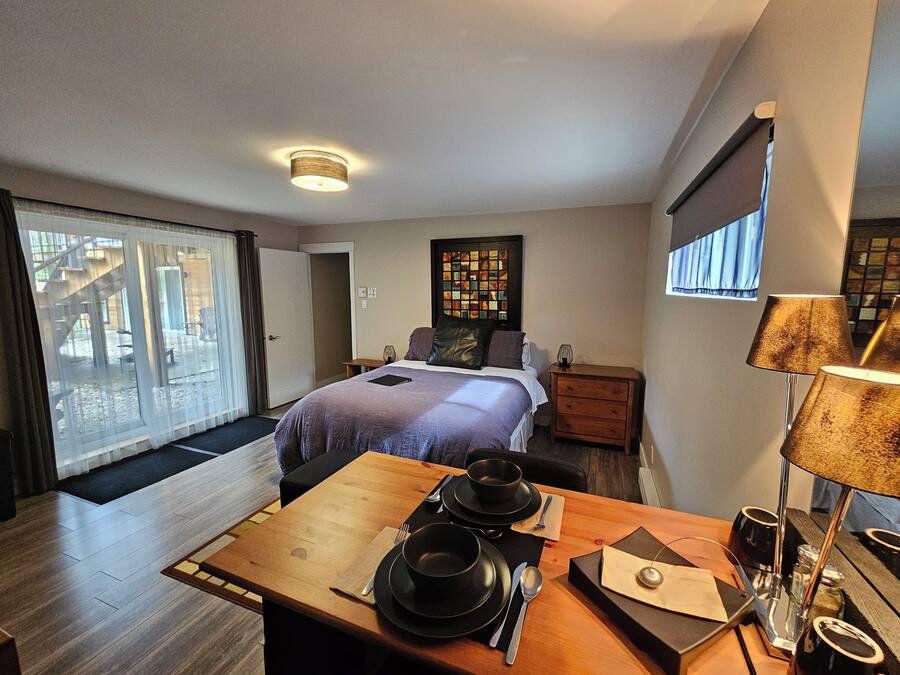 A hotel room with a bed, a small table with a tea set, a nightstand, and a window with curtains.