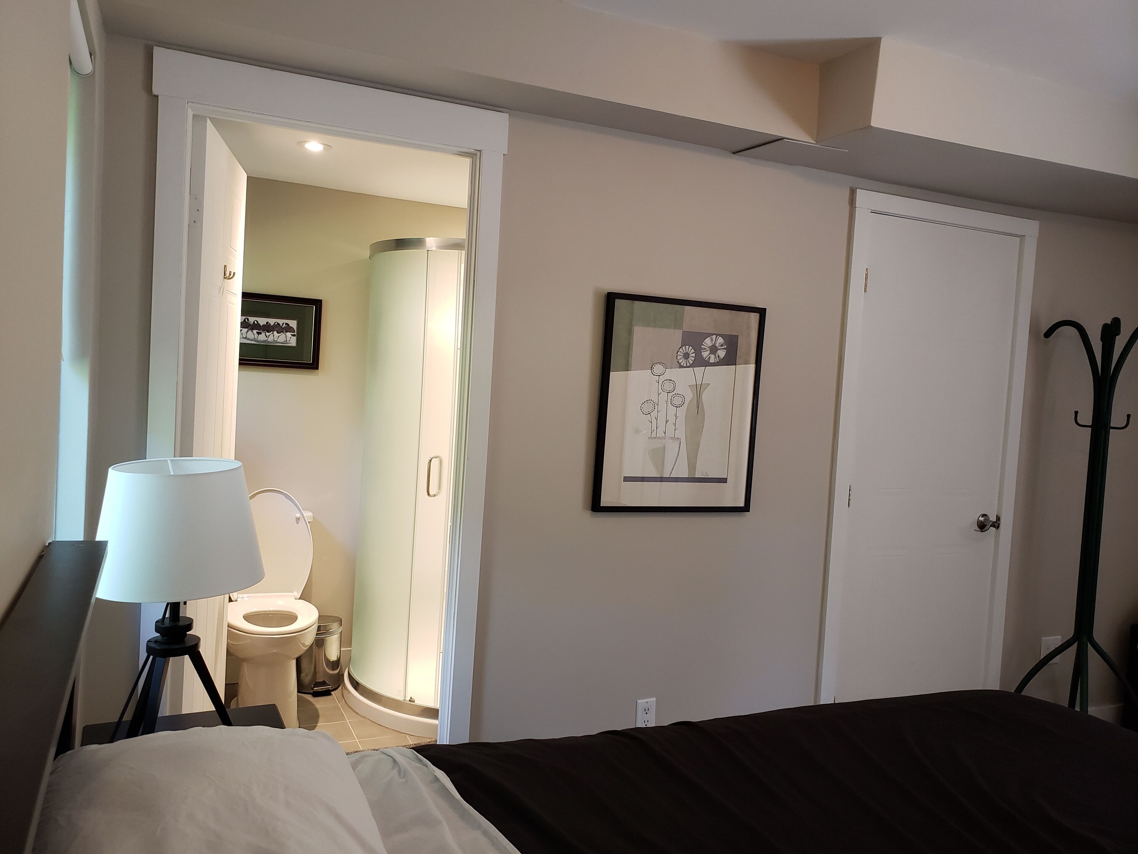 A bedroom with a bed, a bedside lamp, a framed artwork on the wall, and a door leading to a bathroom.