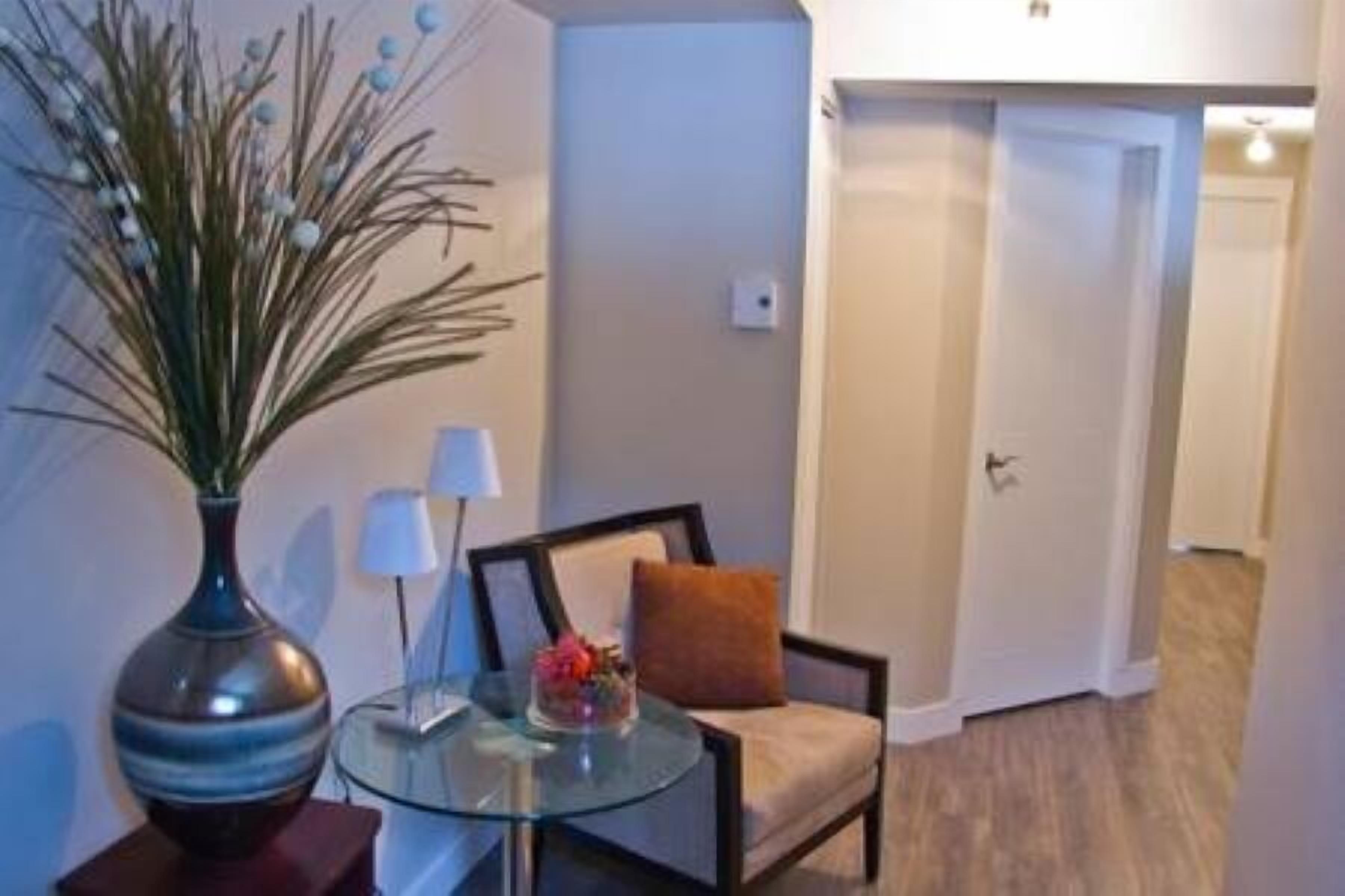 Une petite pièce moderne avec une table en verre, une chaise, un vase avec des plantes et une porte au fond.