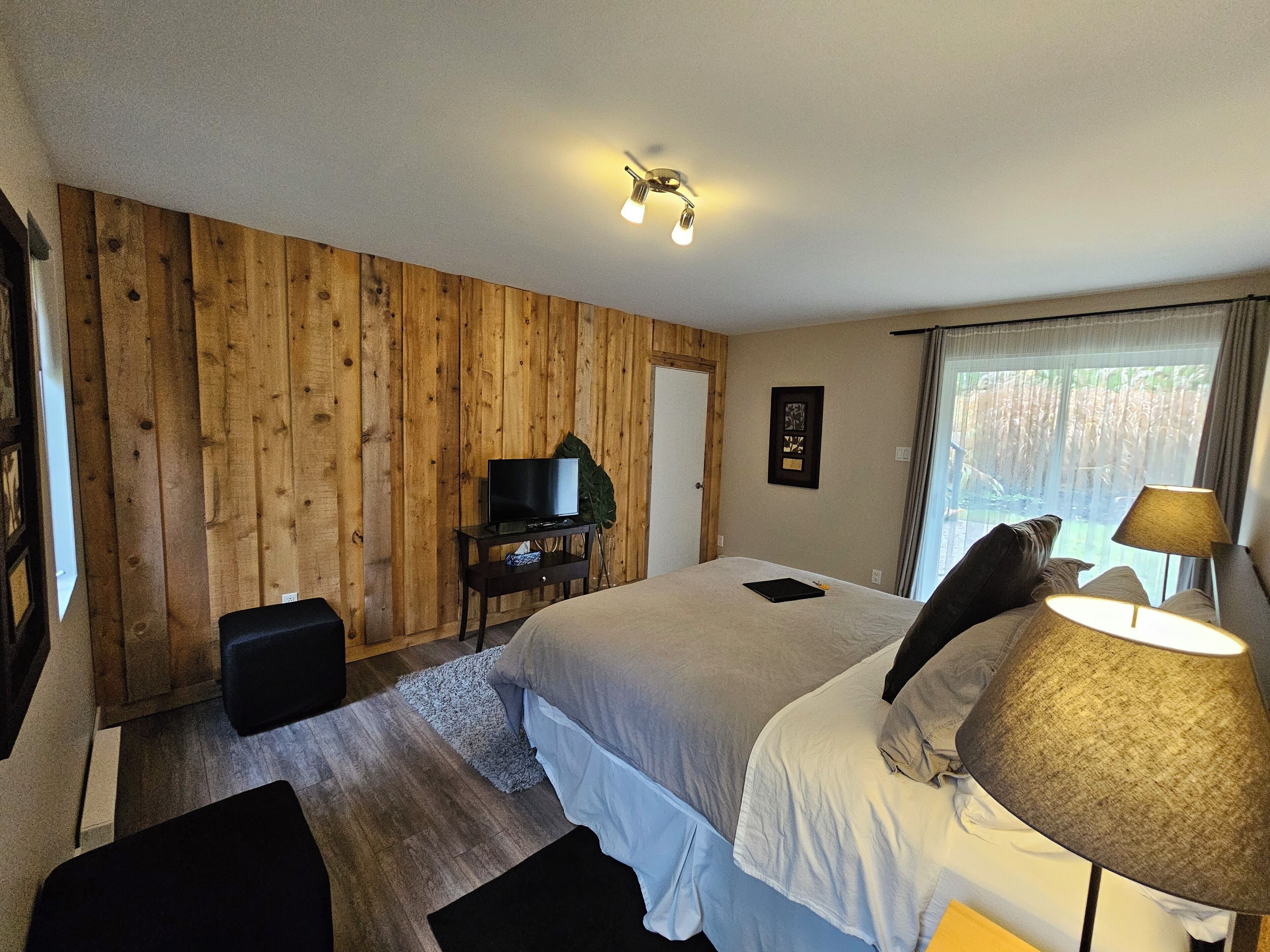 A room with two beds, a TV on a wooden stand, a lamp, and a window with curtains.