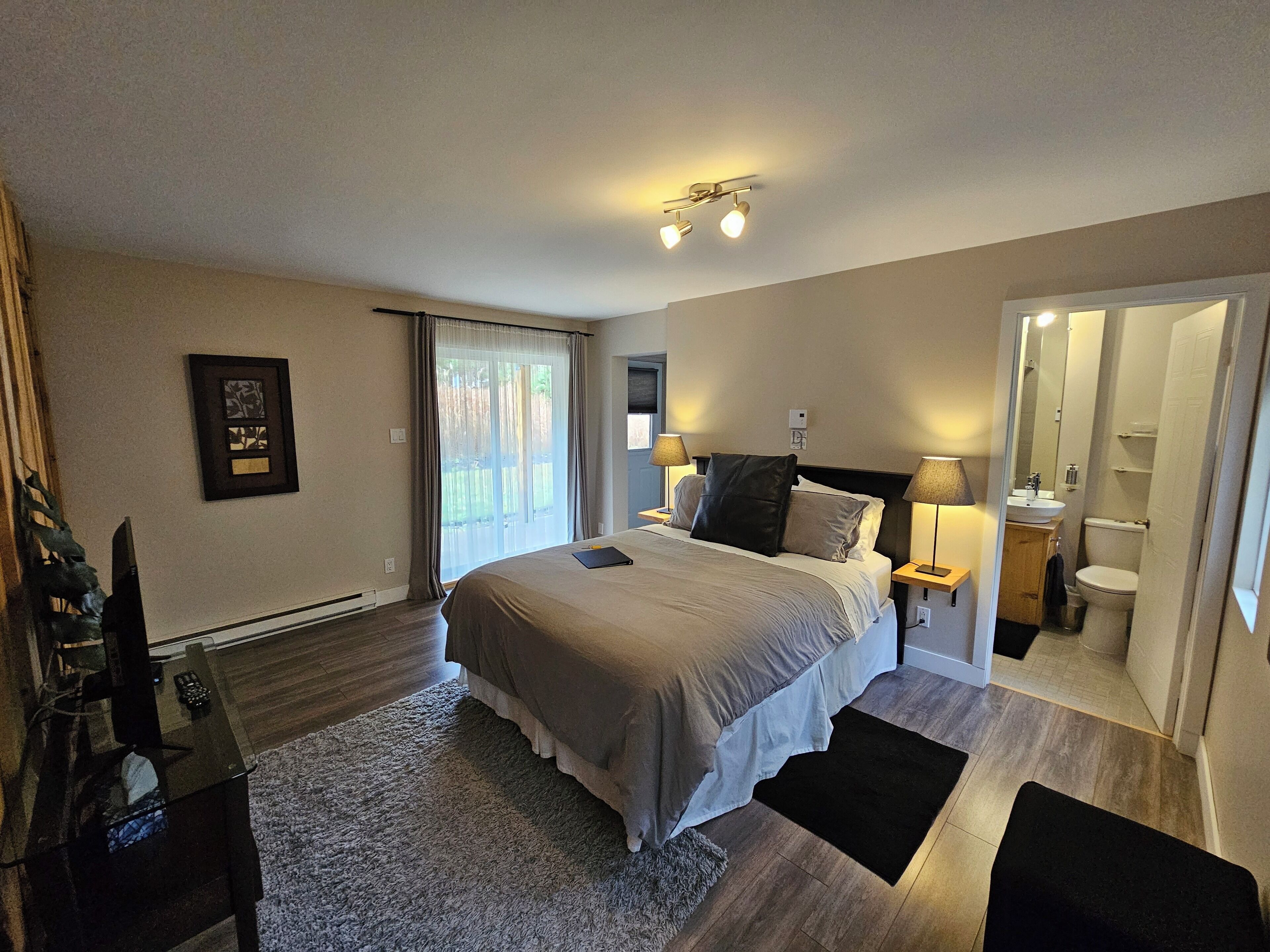 Quarto moderno com uma cama grande, luminárias de cabeceira, uma mesinha e vista para o exterior.