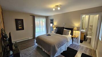 Quarto moderno com uma cama grande, luminárias de cabeceira, uma mesinha e vista para o exterior.