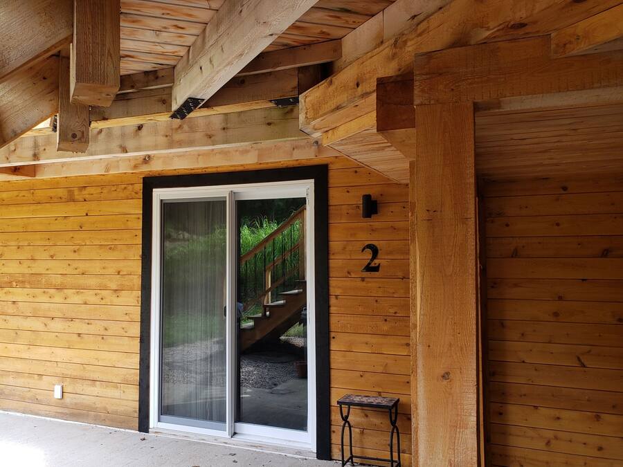 A wooden cabin with a sliding glass door, a small outdoor table, and a staircase leading to a deck.