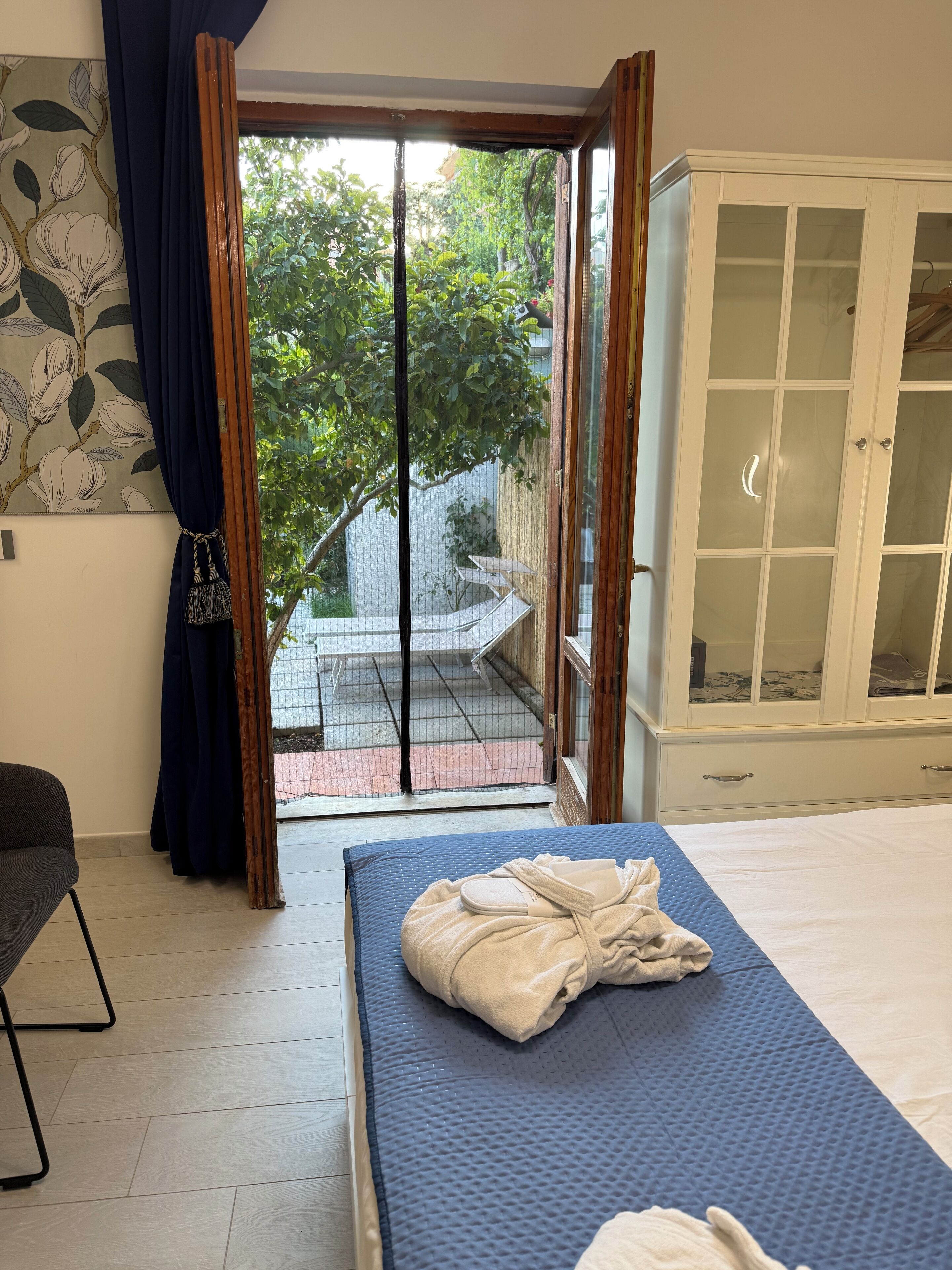 A bedroom with a bed, a wardrobe, a window with curtains, and a view of the outside.