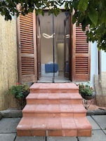 Un conjunto de escalones de terracota que conducen a una puerta de madera con un panel de vidrio, flanqueada por vallas de bambú y plantas en macetas.
