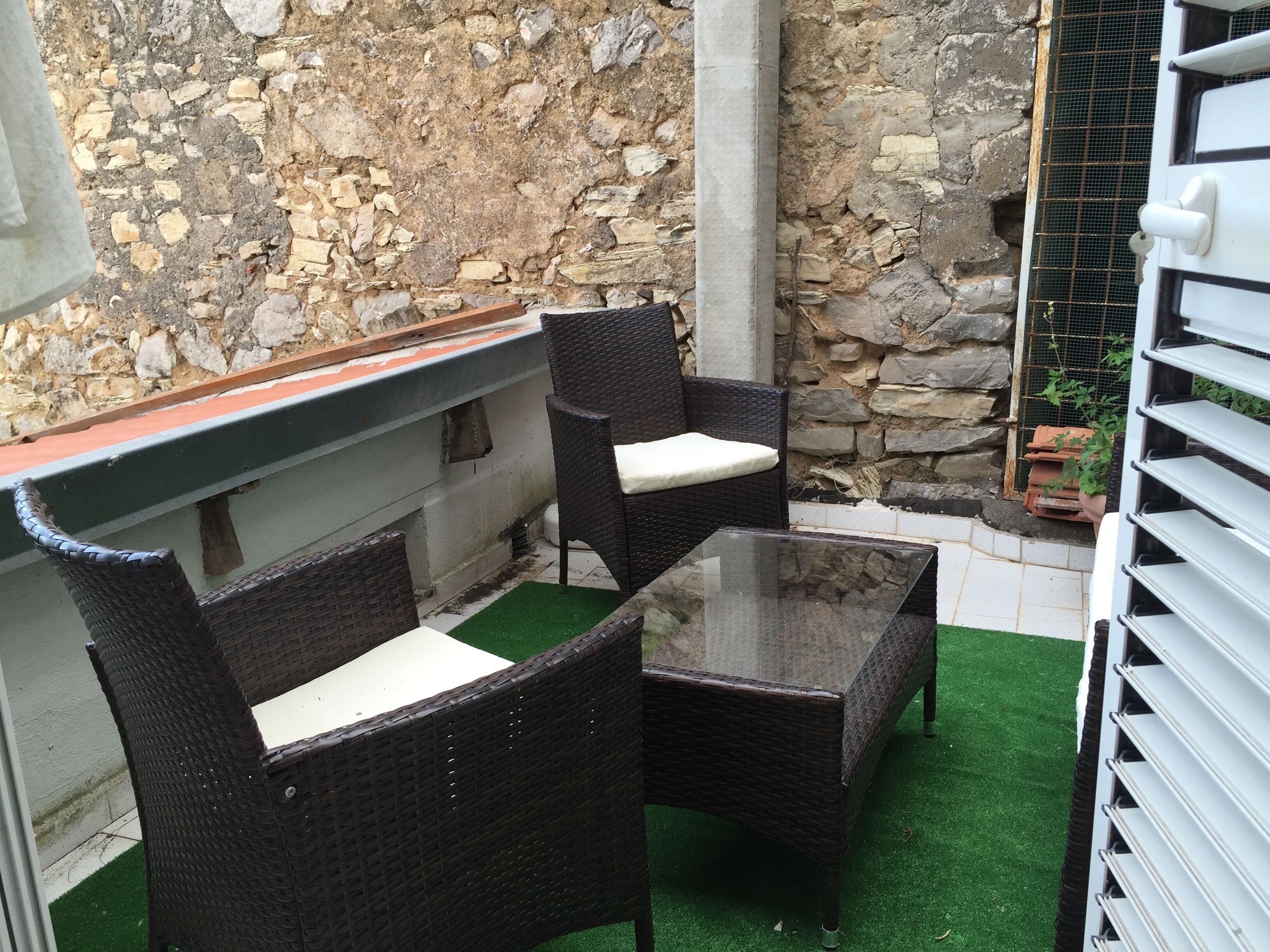 A patio area with wicker furniture, a glass table, and a stone wall backdrop.