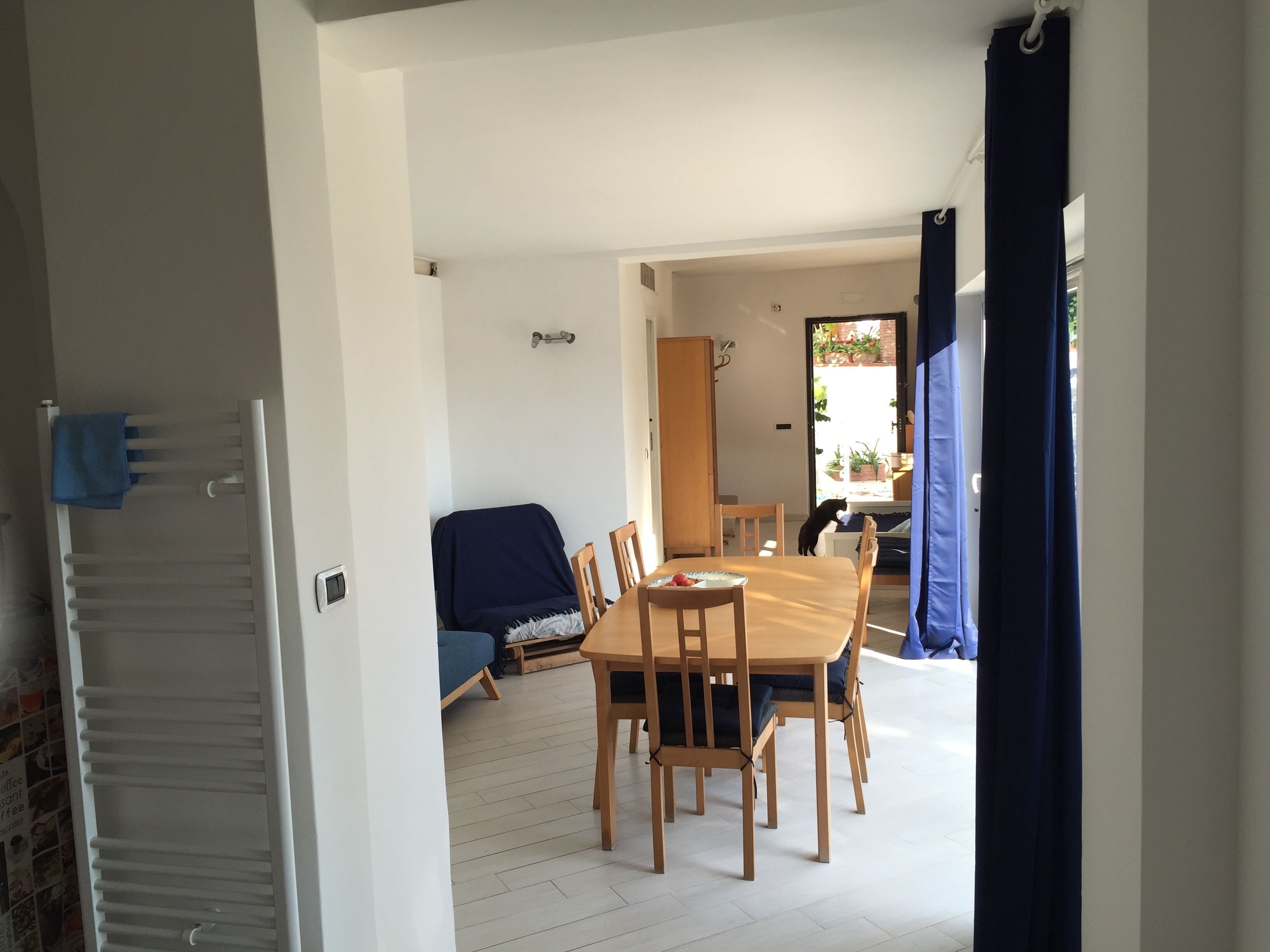 A dining area with a wooden table and chairs, a blue-covered sofa, and a view through a doorway to an outdoor area with plants.