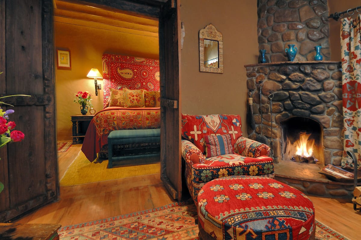 A cozy room with a stone fireplace, a bed with patterned bedding, a chair with a floral cushion, and a vase of flowers.
