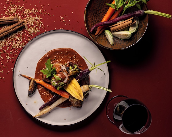 Prato de comida com vários vegetais e um copo de vinho tinto sobre uma mesa vermelha.
