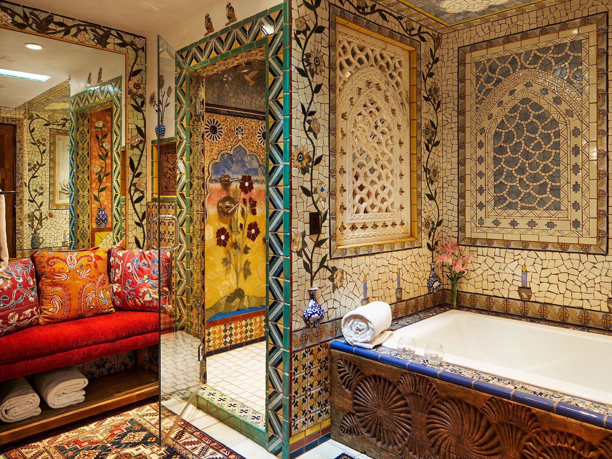 A bathroom with a large bathtub, a mirror, and a red sofa with pillows.