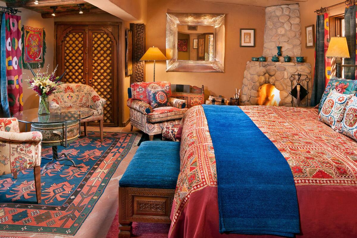 A traditional room with a large bed, two armchairs, a small table, and a fireplace.