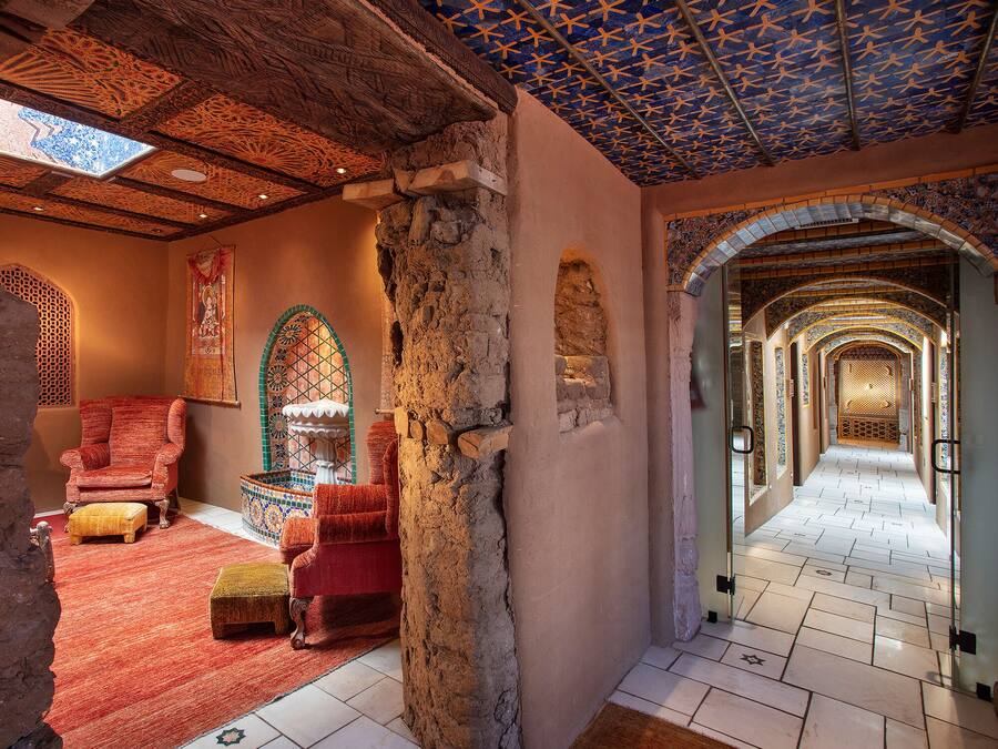Un intérieur traditionnel avec une colonne en pierre, un fauteuil rouge, un tapis à motifs et un couloir carrelé.