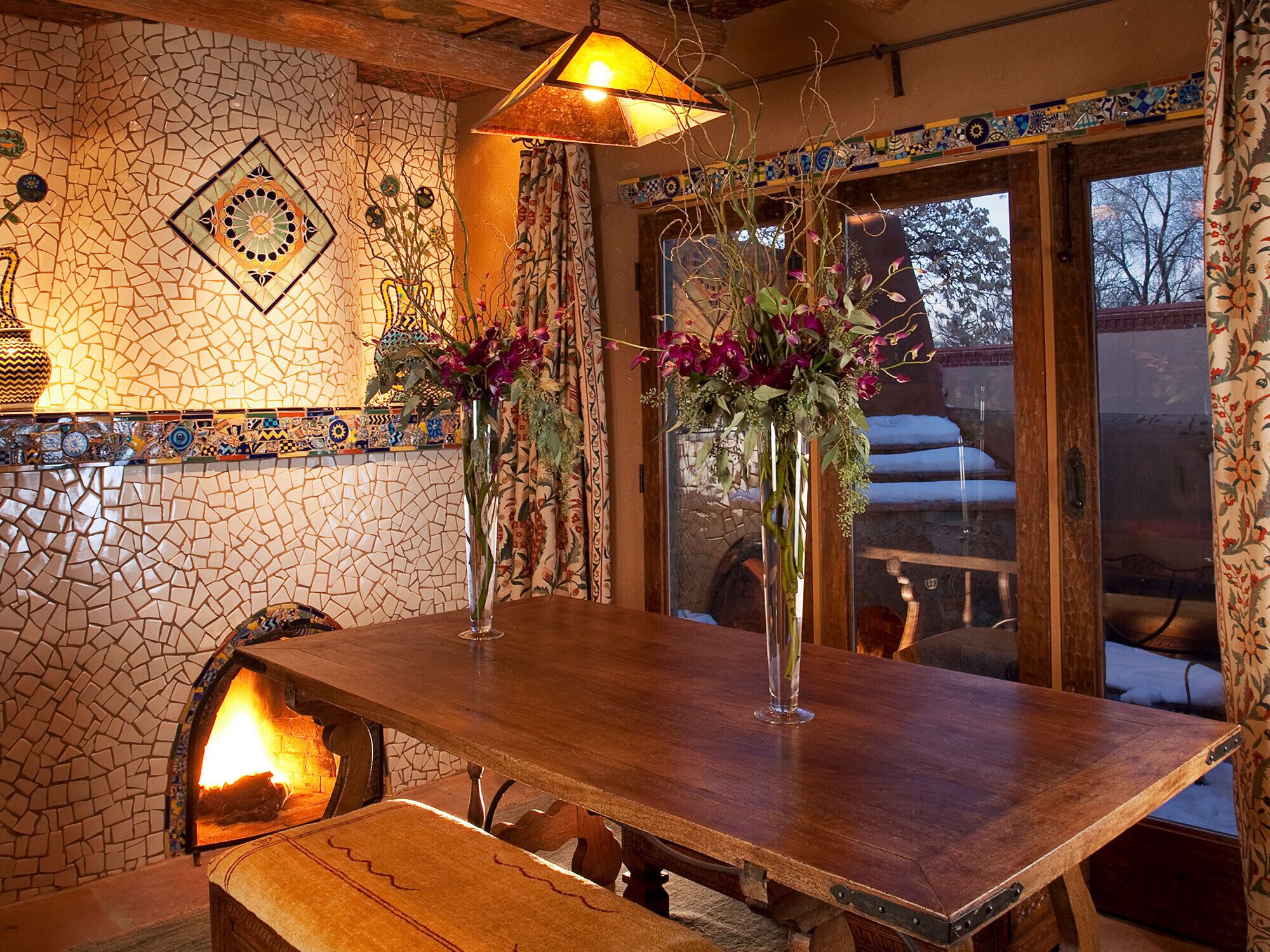Un coin repas rustique avec un mur décoré d’une mosaïque de pierres, une table en bois et une cheminée.