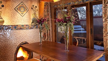 Un coin repas rustique avec un mur décoré d’une mosaïque de pierres, une table en bois et une cheminée.
