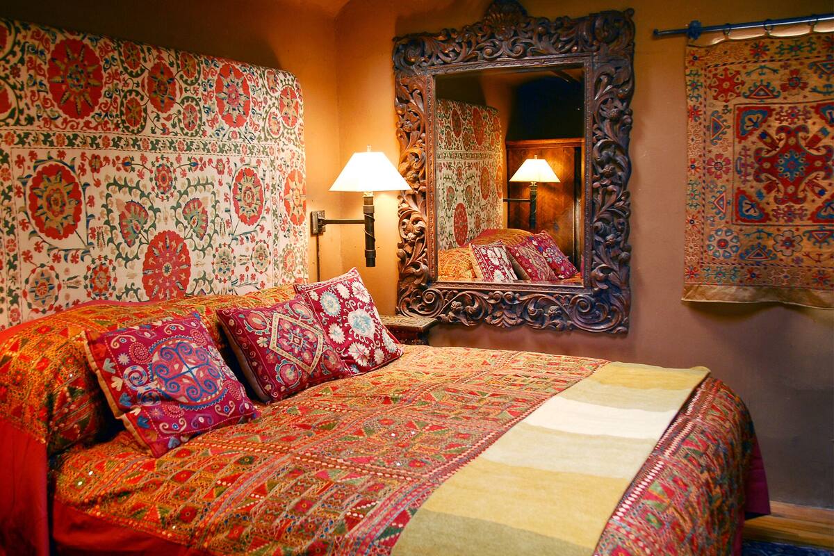 A bed with a patterned bedspread and pillows, a bedside lamp, and a mirror on the wall.