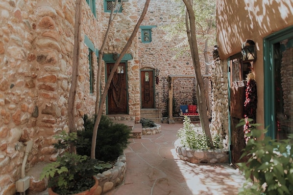 Une cour pavée de pierres, avec un chemin central, entourée de bâtiments aux fenêtres à encadrements verts et aux portes en bois.