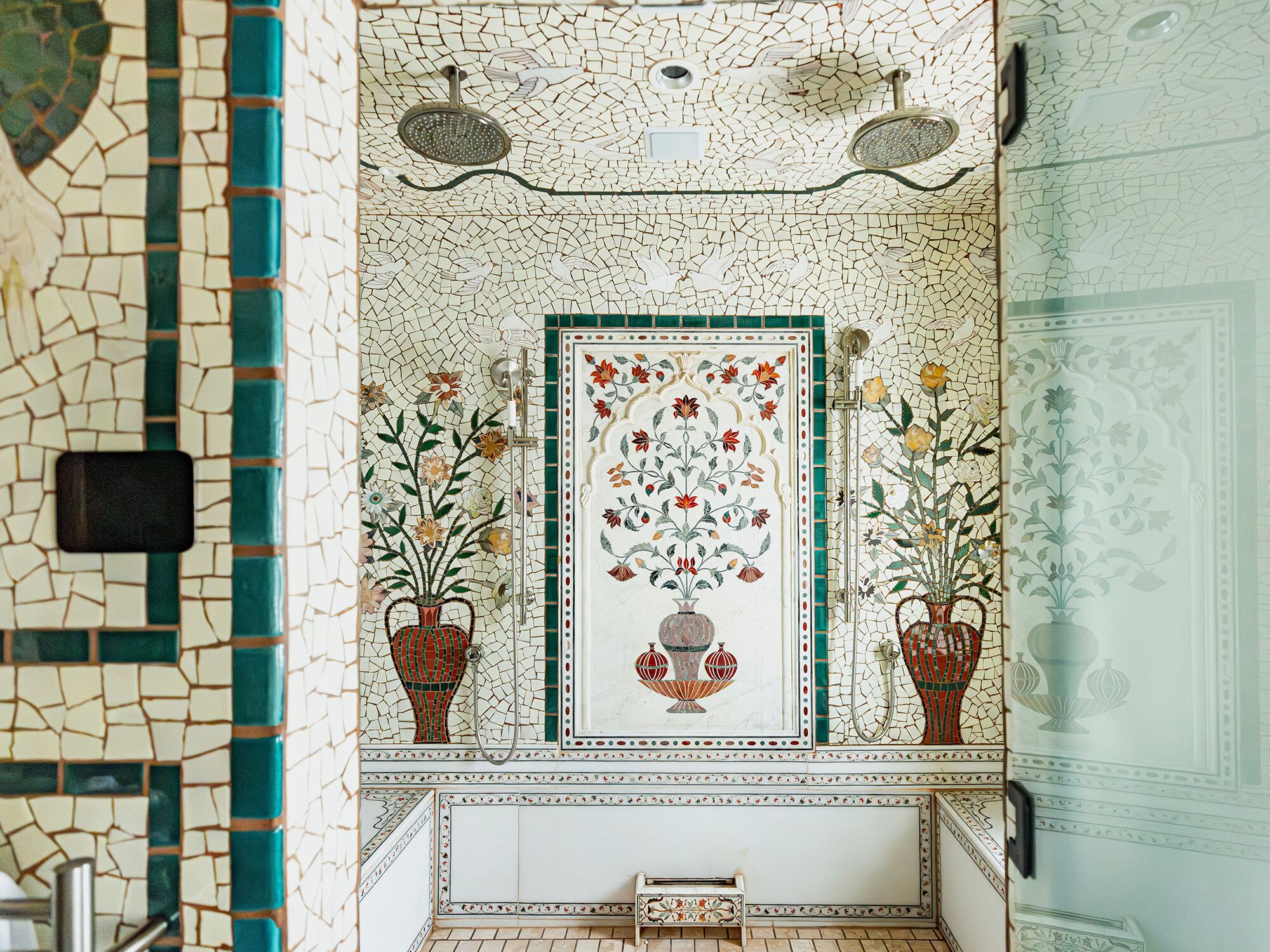 A bathroom with mosaic tile walls, a central floral design, and two potted plants.