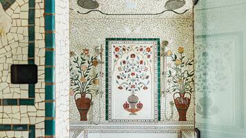 A bathroom with mosaic tile walls, a central floral design, and two potted plants.