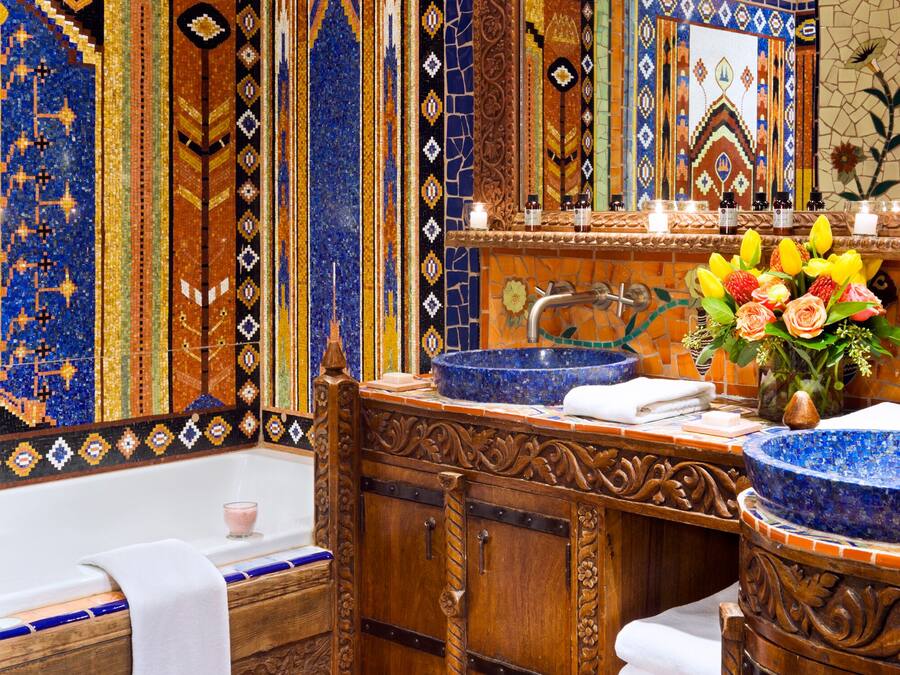 Un baño con una bañera grande, un lavabo con un recipiente azul y un espejo sobre el lavabo. Hay un florero con flores en la encimera del lavabo.