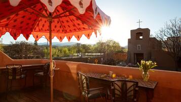 An outdoor patio with wooden furniture, a table with a vase of flowers, and a view of a church and mountains in the background.