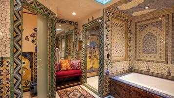 Une salle de bain luxueuse avec une grande baignoire, des carreaux décoratifs et un banc rouge.