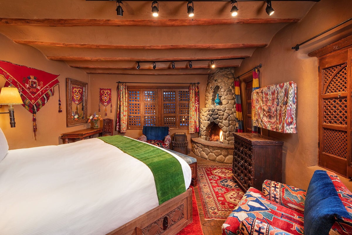 A traditional room with a stone fireplace, a bed with a green throw, and a colorful rug.
