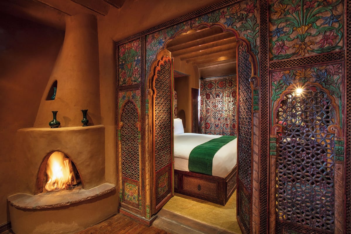 A traditional room with a fireplace, ornate wooden doors, and a bed with a green blanket.
