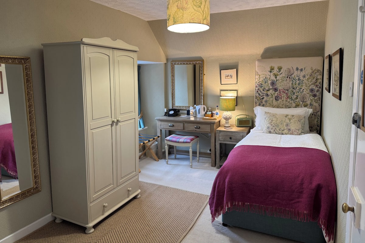 Une chambre à coucher comprenant un lit, un bureau, une armoire, un miroir et une lampe suspendue.
